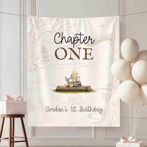 May include: A cream-colored birthday banner with the text "Chapter ONE" in black and brown. The banner features an illustration of Winnie the Pooh and Piglet reading a book. The text "Jordan's 1st Birthday" is also present.