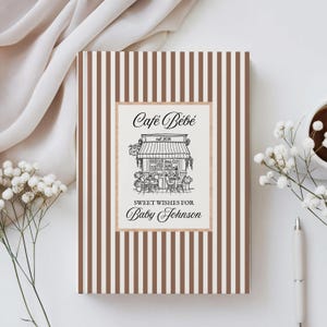 Può includere: Biglietto per baby shower con sfondo a righe marroni e bianche. Il biglietto presenta un'illustrazione incorniciata di un caffè con il testo "Café Bébé" e "Sweet Wishes for Baby Johnson". Una penna, fiori e una tazza di caffè sono sul tavolo.