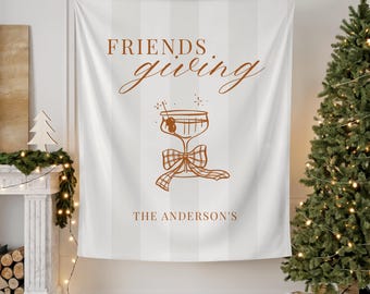 Könnte beinhalten: Ein weißes Friendsgiving-Wandbehang mit vertikalen Streifen und braunem Text. Das Design zeigt die Worte "FRIENDS giving" über einem Cocktailglas mit einer karierten Schleife. Der Familienname "THE ANDERSON'S" ist darunter aufgedruckt.