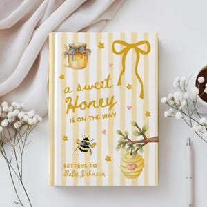 May include: A hardcover baby journal with a yellow and white striped background. The cover features a watercolor illustration of a honey jar, bee, and a beehive. Text reads "a sweet Honey is on the way" and "Letters to Baby Johnson".