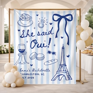 Peut inclure: Une toile de fond à rayures bleues et blanches avec des illustrations sur le thème français, dont la Tour Eiffel et des macarons. Le texte dit "She said Oui!" et "Emma's Bachelorette Charleston, SC July 2026". Des ballons sont au premier plan.