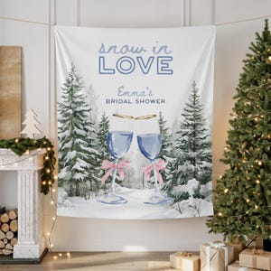 May include: White tapestry featuring a winter forest scene with the text "snow in LOVE" and "Emma's Bridal Shower". Two champagne glasses with pink bows are in the foreground. A Christmas tree and fireplace are in the background.