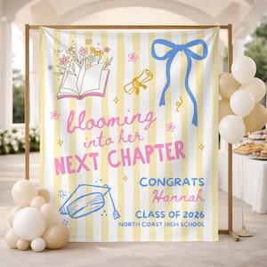 May include: A graduation backdrop with a yellow and white striped background. The backdrop features illustrations of flowers, a book, a diploma, and a graduation cap. Text reads "blooming into her next chapter" and "Congrats Hannah, Class of 2026, North Coast High School."