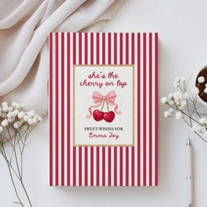 Op de afbeelding: Een wenskaart met een rood en wit gestreepte achtergrond. De kaart heeft een centraal rechthoekig ontwerp met een roze strik en twee kersen. De tekst luidt "she's the cherry on top" en "Sweet Wishes for Emma Joy."