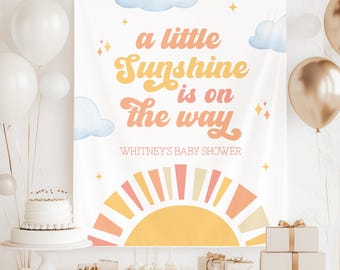 Puede incluir: Un telón de fondo rectangular blanco con el texto 'a little Sunshine is on the way' en letras naranjas y amarillas, y 'WHITNEY'S BABY SHOWER' debajo. El diseño incluye nubes azul claro, estrellas amarillas y un sol.
