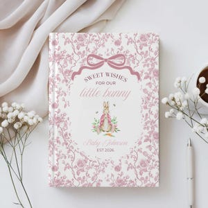 Może przedstawiać: Twarda oprawa dziennika dla dziecka z różowym wzorem kwiatowym. Okładka zawiera napis "Sweet Wishes for our little bunny" z akwarelową ilustracją królika w różowej kurtce. Imię i rok dziecka są również wydrukowane.