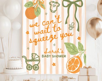 Puede incluir: Una pancarta de baby shower con rayas naranjas y blancas, con ilustraciones de naranjas y el texto "we can't wait to squeeze you". La pancarta también incluye un cochecito, un body y un chupete.