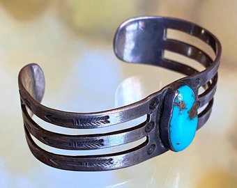 May include: A silver bracelet with three bands and a turquoise stone. The bands are decorated with arrow designs.
