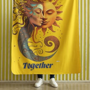 May include: Yellow throw blanket with a sun and moon design. The sun and moon are depicted as faces, with the sun having a yellow face and the moon having a blue face. The text "Together" is printed in blue at the bottom of the blanket.