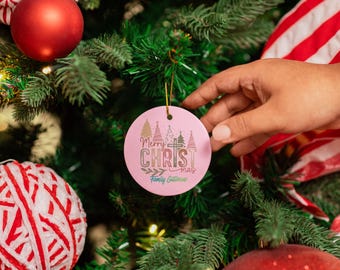 May include: A pink Christmas ornament with the text "Merry CHRISTmas Family Gatherers" and tree and cross graphics. The ornament is hanging on a green Christmas tree with red ornaments and a red and white striped decoration.
