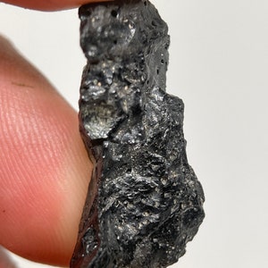 May include: A dark gray, rough, and textured rock with small, white flecks throughout.