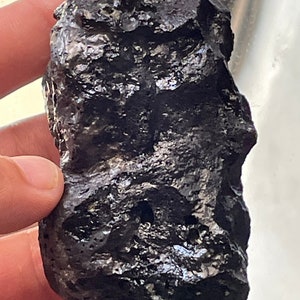 May include: A dark gray, rough, and irregularly shaped rock with a metallic sheen.