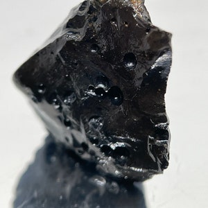 May include: A black, rough, and porous rock with a smooth, shiny surface. The rock has a unique, irregular shape and appears to be volcanic in origin.