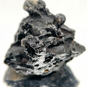May include: A black, irregularly shaped rock with a rough, textured surface. The rock has a small, round protrusion on top.