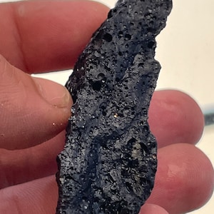 May include: A dark gray, rough, and porous volcanic rock with a unique shape.