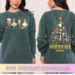 Puede incluir: Una sudadera verde oscuro con temática de Cascanueces. La parte delantera muestra cuatro personajes de Cascanueces. La parte trasera presenta un diseño de árbol de Navidad con figuras de Cascanueces y el texto "Nutcracker Season".
