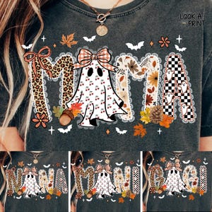 Puede incluir: Camiseta gris oscuro con la palabra "MAMA" en un diseño decorativo. La "M" es de estampado de leopardo, la "A" es un fantasma con detalles de cerezas, y las otras letras tienen patrones florales y a cuadros. También se presentan hojas de otoño y murciélagos.