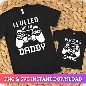 Puede incluir: Dos camisetas negras con texto blanco y gráficos de mando. Una camiseta dice "LEVELED UP TO DADDY". La otra dice "PLAYER 2 has entered the GAME". La parte inferior de la imagen tiene el texto "PNG & SVG INSTANT DOWNLOAD."
