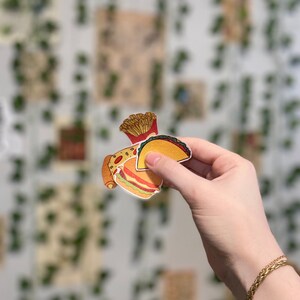 May include: A set of three food-themed stickers featuring a hamburger, a taco, and french fries. The stickers are printed on white paper and have a cartoon-like style.