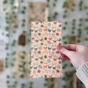 Pu&ograve; includere: Un foglio di carta rosa con un motivo ripetitivo di farfalle e fiori. Le farfalle sono blu, arancioni e gialle. I fiori sono rosa, blu e gialli.