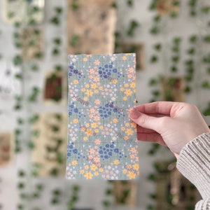 Pu&ograve; includere: Un tessuto blu e bianco con un motivo floreale. Il tessuto &egrave; ricoperto di piccoli fiori gialli, rosa e blu.
