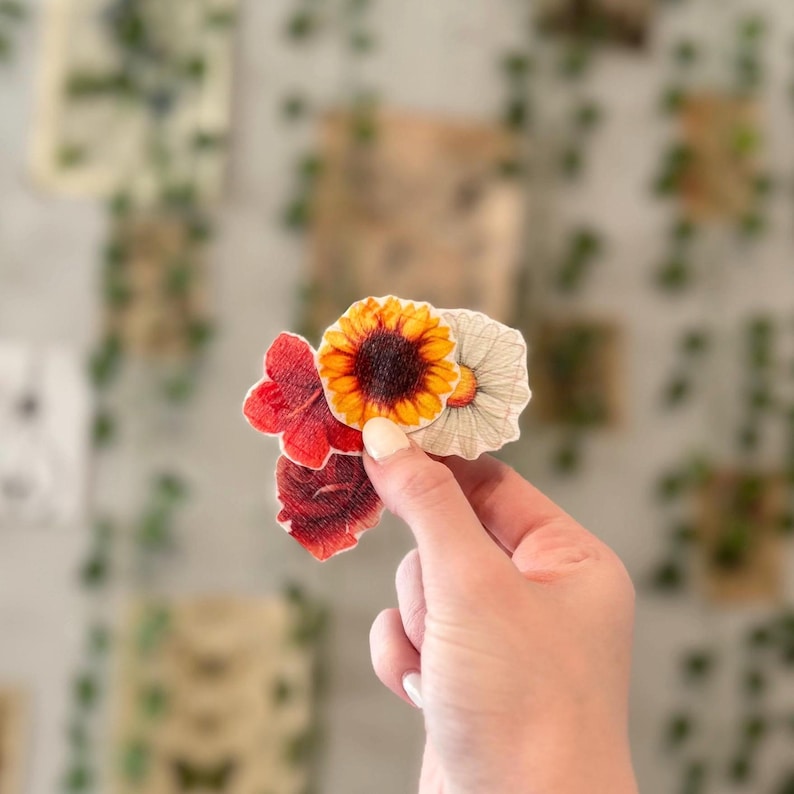 May include: Three paper flower stickers, one red, one yellow with a brown center, and one white with a yellow center.