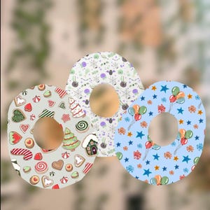 May include: Three decorative donut-shaped items with different patterns. One has a light gray background with gingerbread cookies, another has a white background with Halloween-themed designs, and the last has a light blue background with balloons and stars.