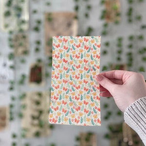 Pu&ograve; includere: Un tessuto bianco con un motivo ripetitivo di farfalle colorate e foglie verdi. Il tessuto &egrave; di forma quadrata ed &egrave; tenuto da una mano.