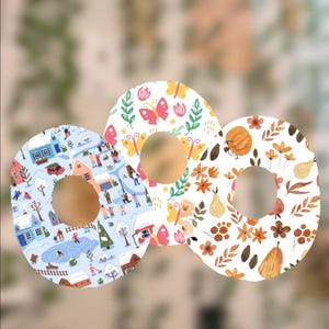 May include: Three decorative round coasters with different patterns. One features a winter scene with houses and people ice skating. Another has butterflies and flowers. The third has pumpkins and fall foliage.