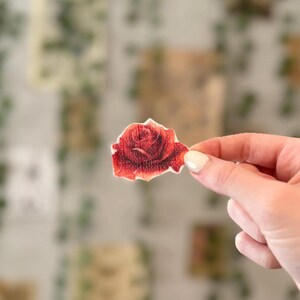 May include: A red rose flower printed on a white fabric patch.