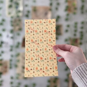 Pu&ograve; includere: Un foglio di carta da forno in cera d'api gialla con un motivo ripetitivo di api, fiori e foglie. La carta &egrave; leggermente stropicciata e ha una superficie testurizzata.