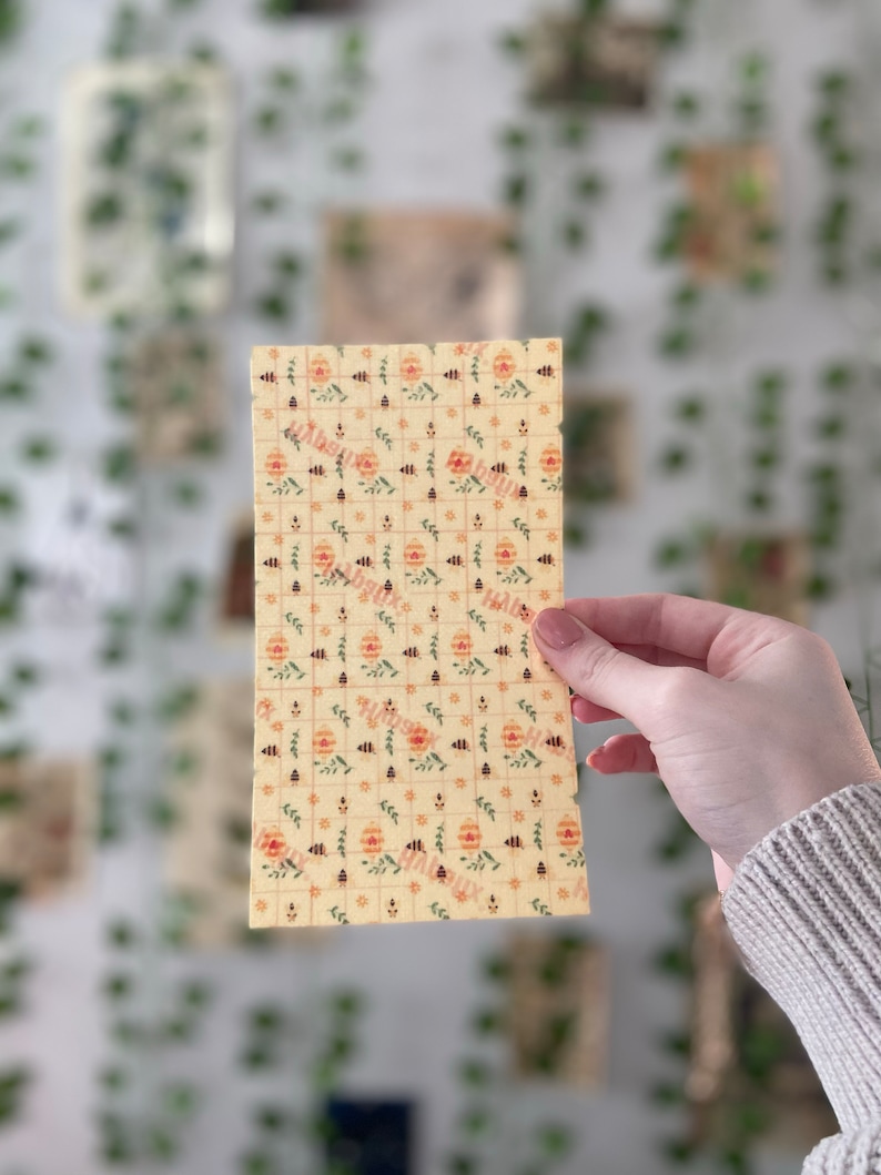 Pu&ograve; includere: Un foglio di carta da forno in cera d'api gialla con un motivo ripetitivo di api, fiori e foglie. La carta &egrave; leggermente stropicciata e ha una superficie testurizzata.
