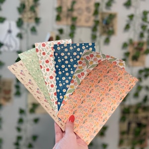 May include: A set of seven floral patterned wrapping paper sheets in various colors, including green, red, blue, and peach. The sheets are arranged in a fan shape, with the peach sheet on top.