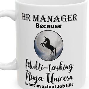 May include: White ceramic coffee mug with black text that reads "HR MANAGER Because Multi-tasking Ninja Unicorn is not an actual job title". A black silhouette of a unicorn is in the center of the mug against a white moon background.