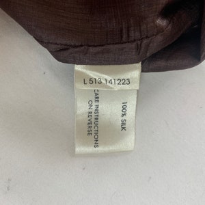 Puede incluir: Etiqueta blanca con texto negro que dice "L 513 141223", "CARE INSTRUCTIONS ON REVERSE" y "100% SILK".