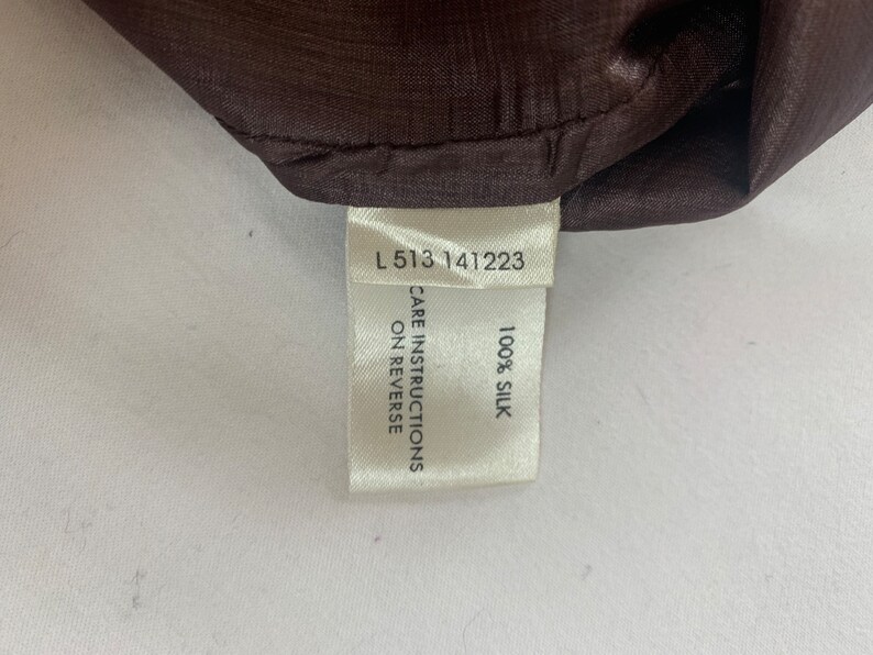 Puede incluir: Etiqueta blanca con texto negro que dice "L 513 141223", "CARE INSTRUCTIONS ON REVERSE" y "100% SILK".