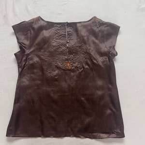Puede incluir: Una blusa de seda marr&oacute;n con mangas cortas y detalles bordados. La blusa tiene un escote redondo y un cierre de bot&oacute;n en la espalda.