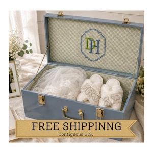 May include: A light blue wooden keepsake box with gold-tone metal latches and handle. The interior is lined with a patterned fabric featuring an embroidered monogram of the letters DH. Inside are white faux fur slippers and a white lace veil.