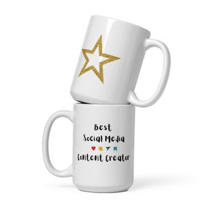 May include: Two white ceramic mugs stacked on top of each other. The top mug has a gold glitter star design. The bottom mug has the text "Best Social Media Content Creator" with a heart, speech bubble, and flag icons.
