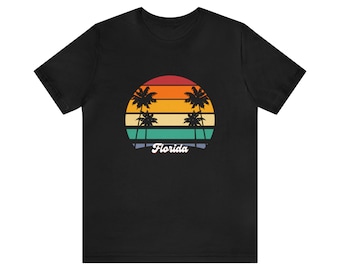 Puede incluir: Camiseta negra con un gráfico de puesta de sol retro con palmeras y la palabra "Florida" en una fuente vintage.