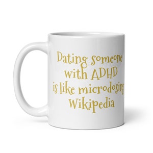 May include: White ceramic coffee mug with a gold inscription that reads "Dating someone with ADHD is like microdosing Wikipedia."