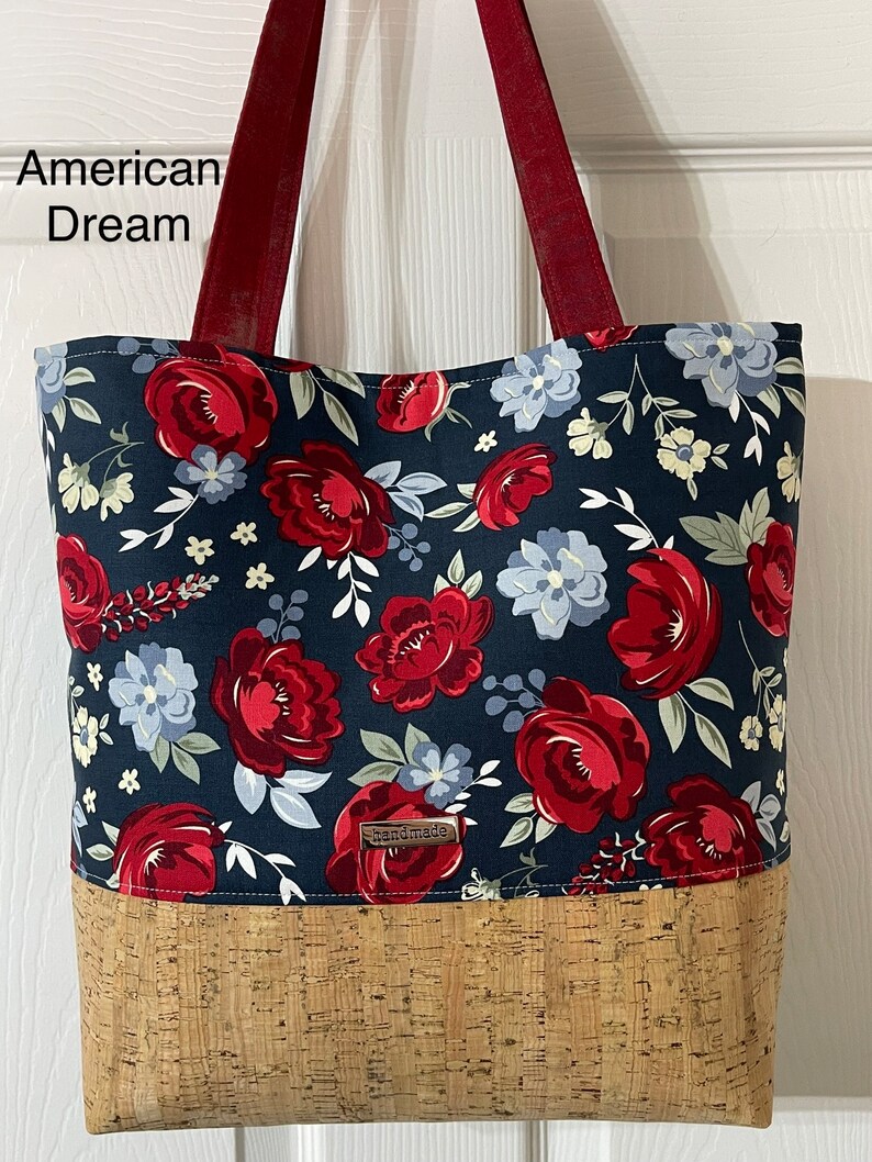 K&ouml;nnte beinhalten: Eine marineblaue Tragetasche mit rotem und wei&szlig;em Blumendruck. Die Tasche hat einen Korkboden und rote Henkel. Die Tasche hat ein kleines braunes Etikett mit der Aufschrift "handgefertigt".