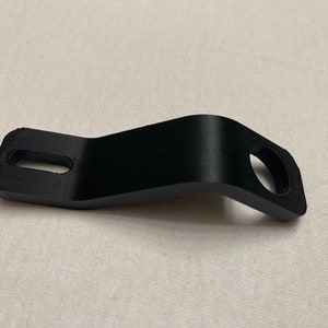 Puede incluir: Soporte de plástico negro con dos agujeros, uno ovalado y otro redondo.