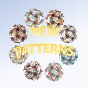May include: Eight colorful paper sphere lamps with different patterns, including paw prints, rainbows, and geometric designs. The lamps are arranged in a circle with the text "NEW PATTERNS" in the center.