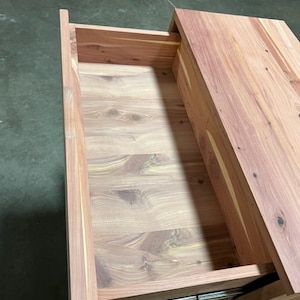 May include: A wooden drawer with a light brown finish. The drawer is open and the inside is visible. The drawer is made of wood with a natural grain pattern.