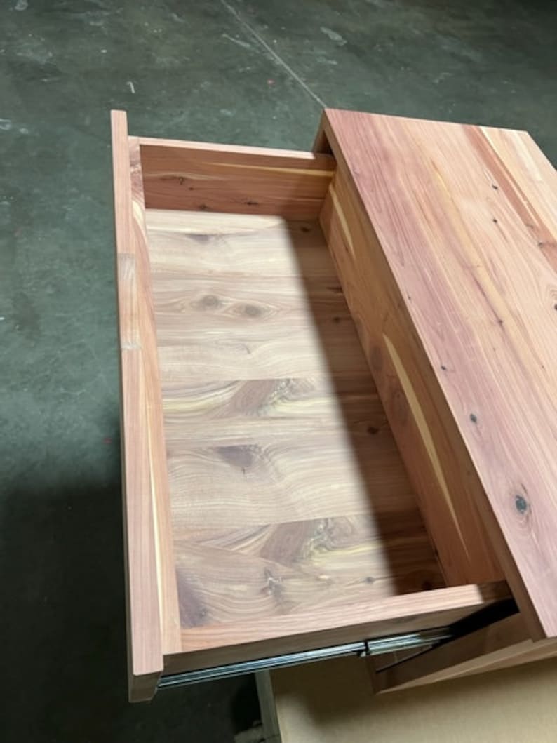 May include: A wooden drawer with a light brown finish. The drawer is open and the inside is visible. The drawer is made of wood with a natural grain pattern.