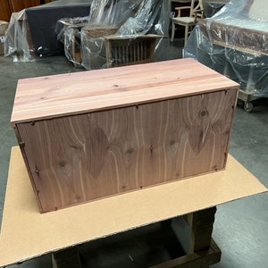 May include: A wooden storage box with a natural wood finish. The box has a rectangular shape and is made of solid wood.