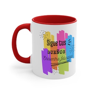 May include: White ceramic coffee mug with a red rim. The mug features a colourful abstract design with the text "Sigue tus sueños Encuentra felicidad".