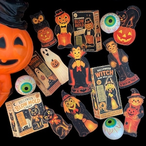 May include: A collection of vintage-style Halloween blow mold lights and their original boxes, featuring figures of a pumpkin, owl, ghost, vampire, witch, black cat, and scarecrow, alongside several round, white, and green eyeball decorations.