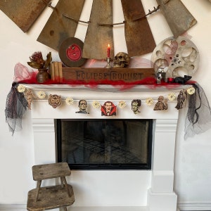 May include: A white fireplace mantel decorated with a black and white Halloween garland featuring various monster characters. The garland is strung with black and white ribbon and hangs above a black fireplace.